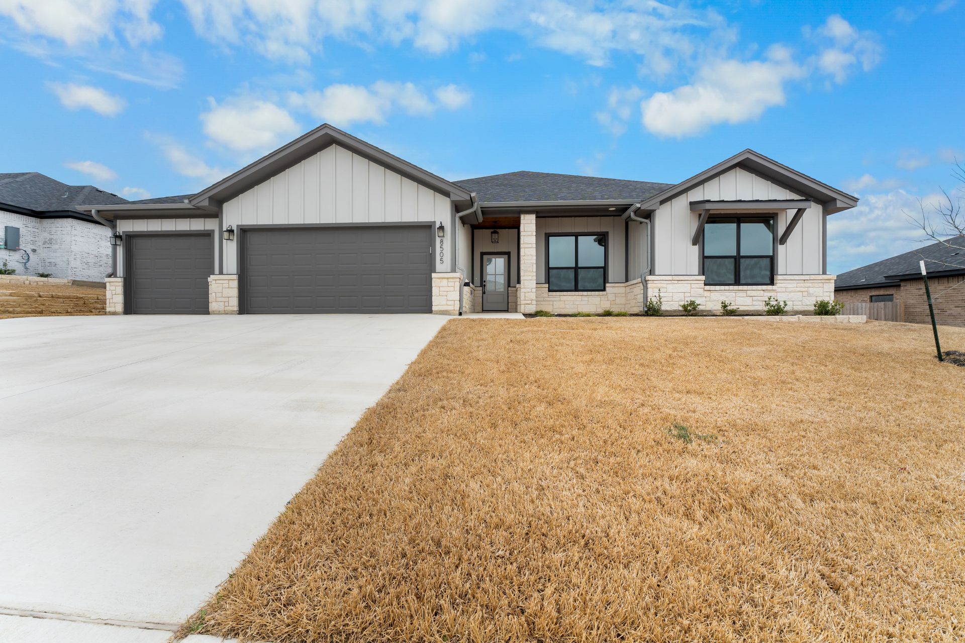 Modern one-story house with a gray exterior and a brown yard under a blue sky.