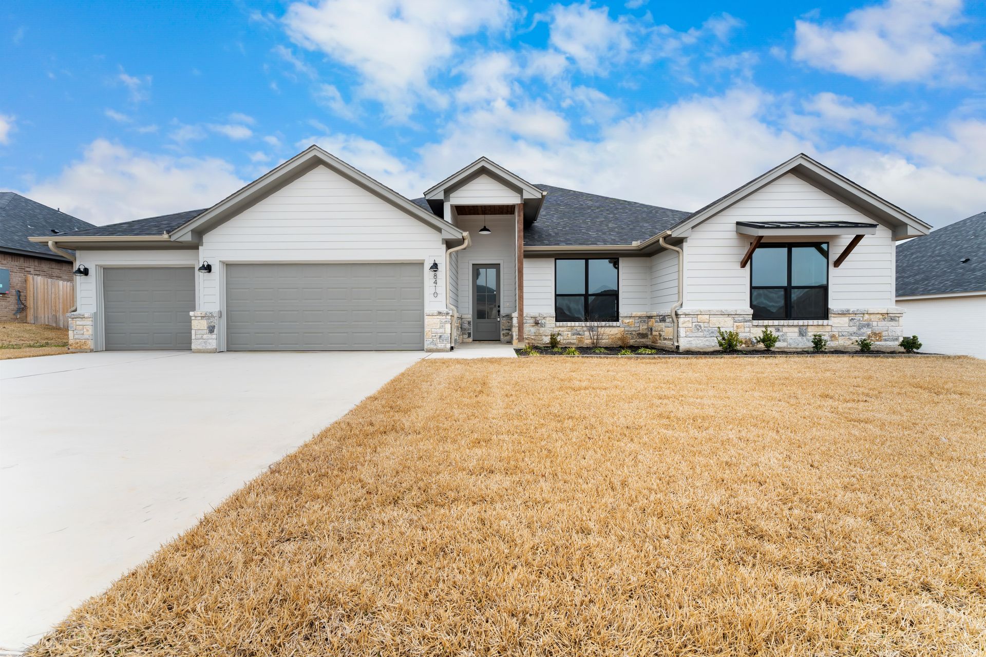 White suburban house with gray garage doors and brown dry grass.