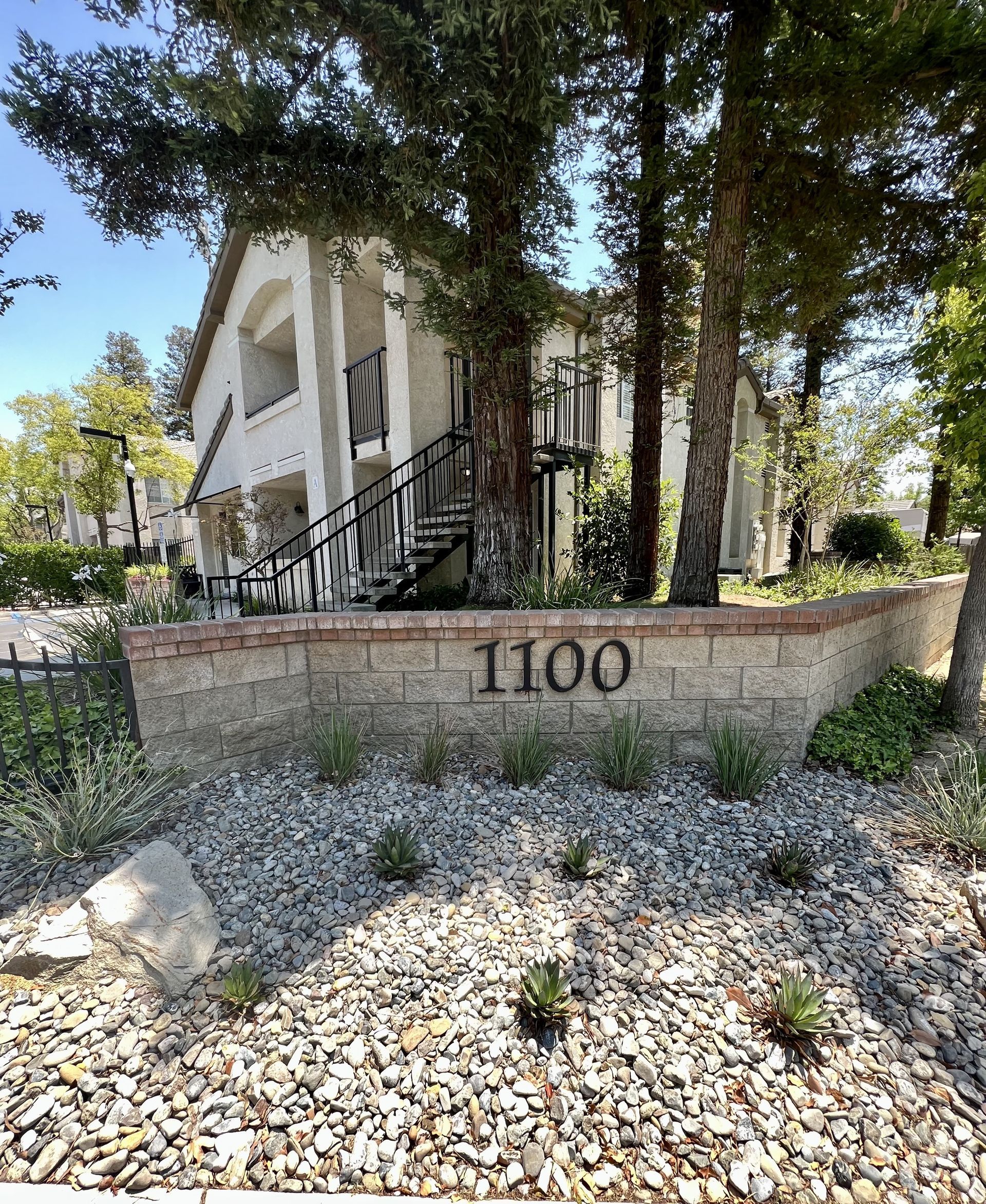 A building with a sign that says 1100 on it is surrounded by trees and rocks.