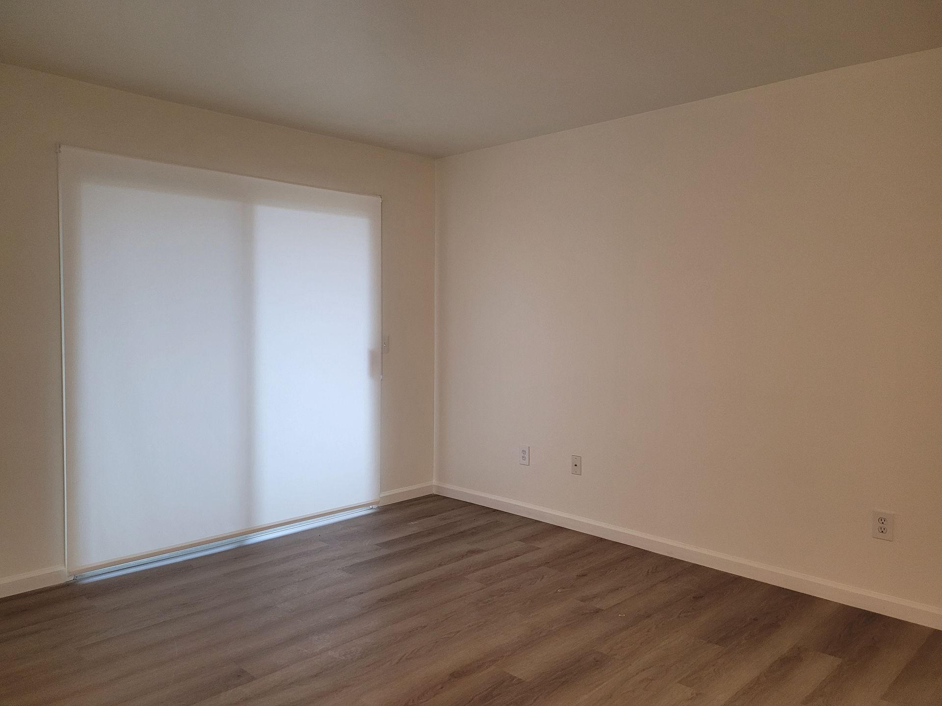 An empty room with a sliding glass door and hardwood floors.