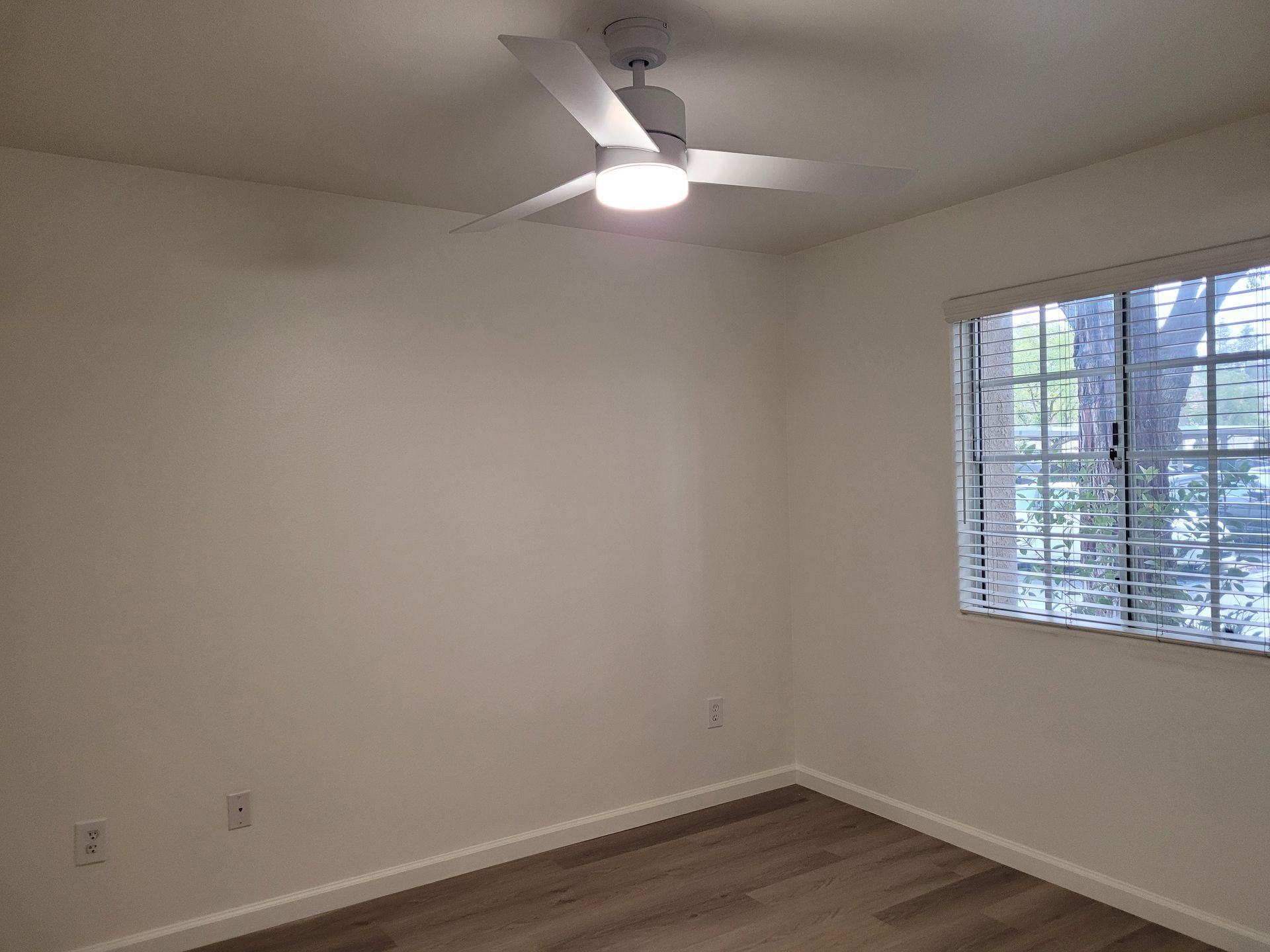 An empty bedroom with a ceiling fan and a window.