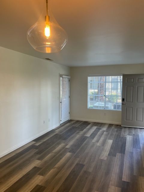 An empty living room with hardwood floors and a light hanging from the ceiling.