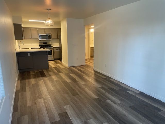 A living room with hardwood floors and a kitchen in the background