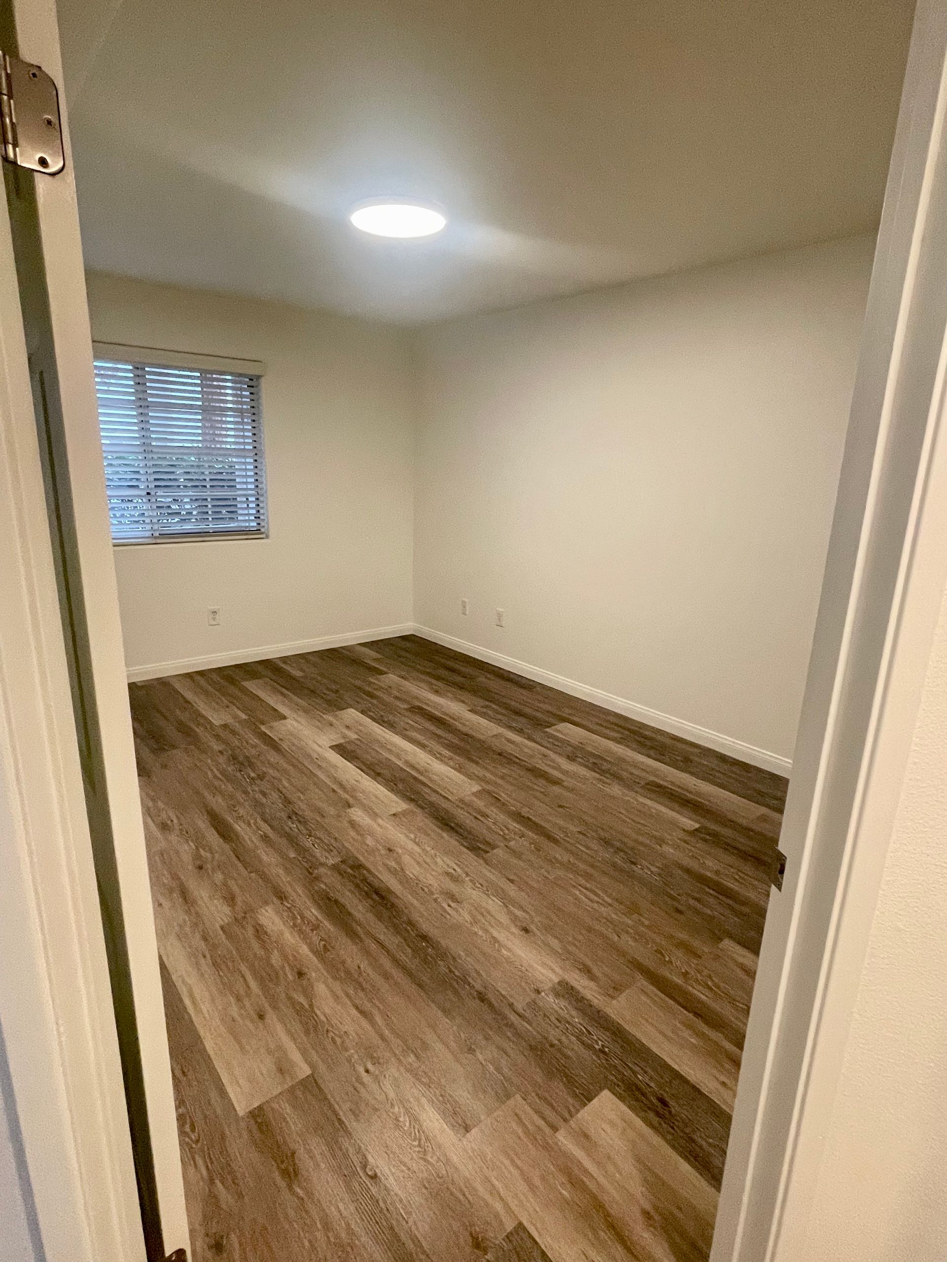 A bedroom with hardwood floors and a window.