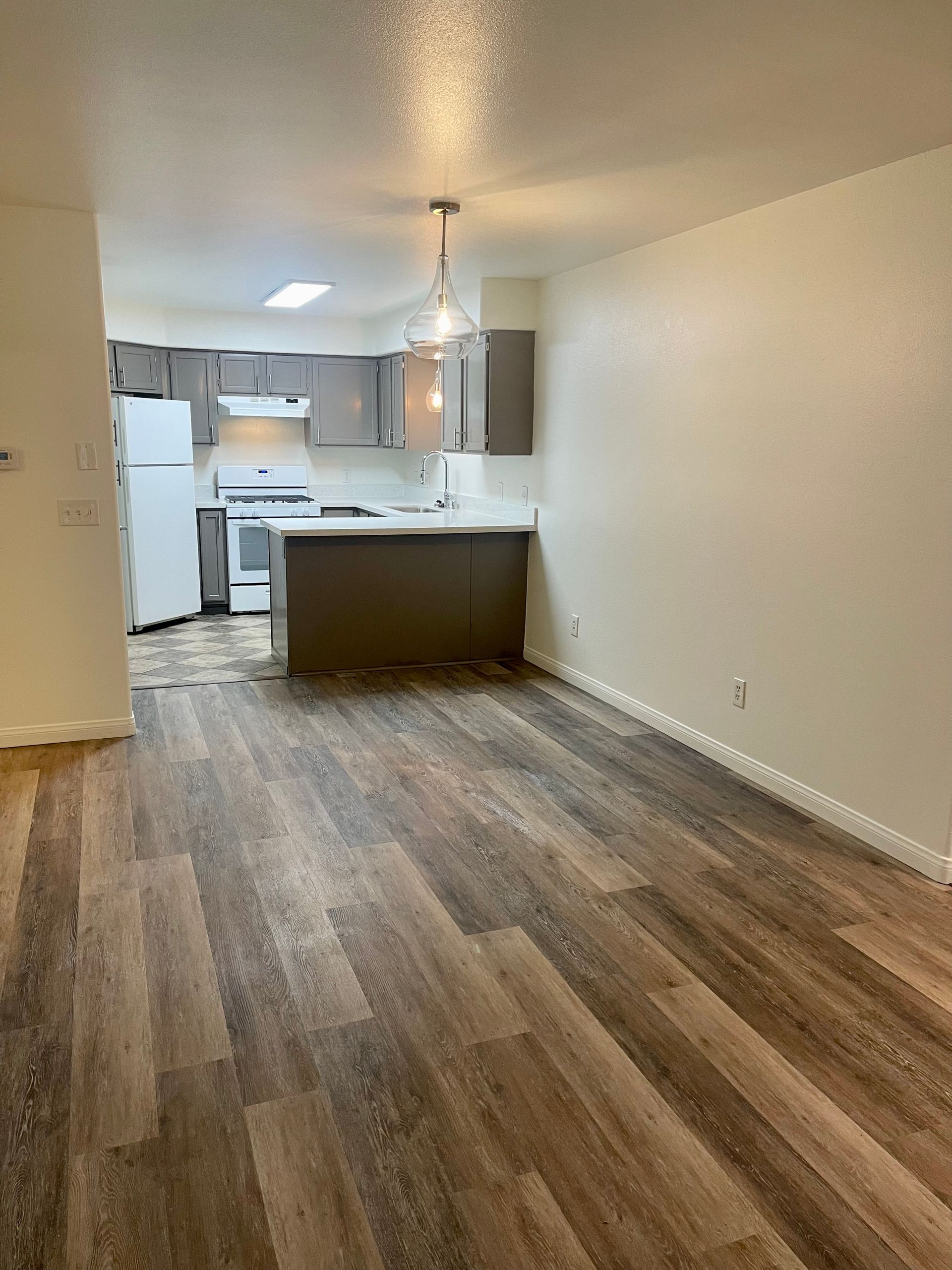 A living room with hardwood floors and a kitchen in the background.