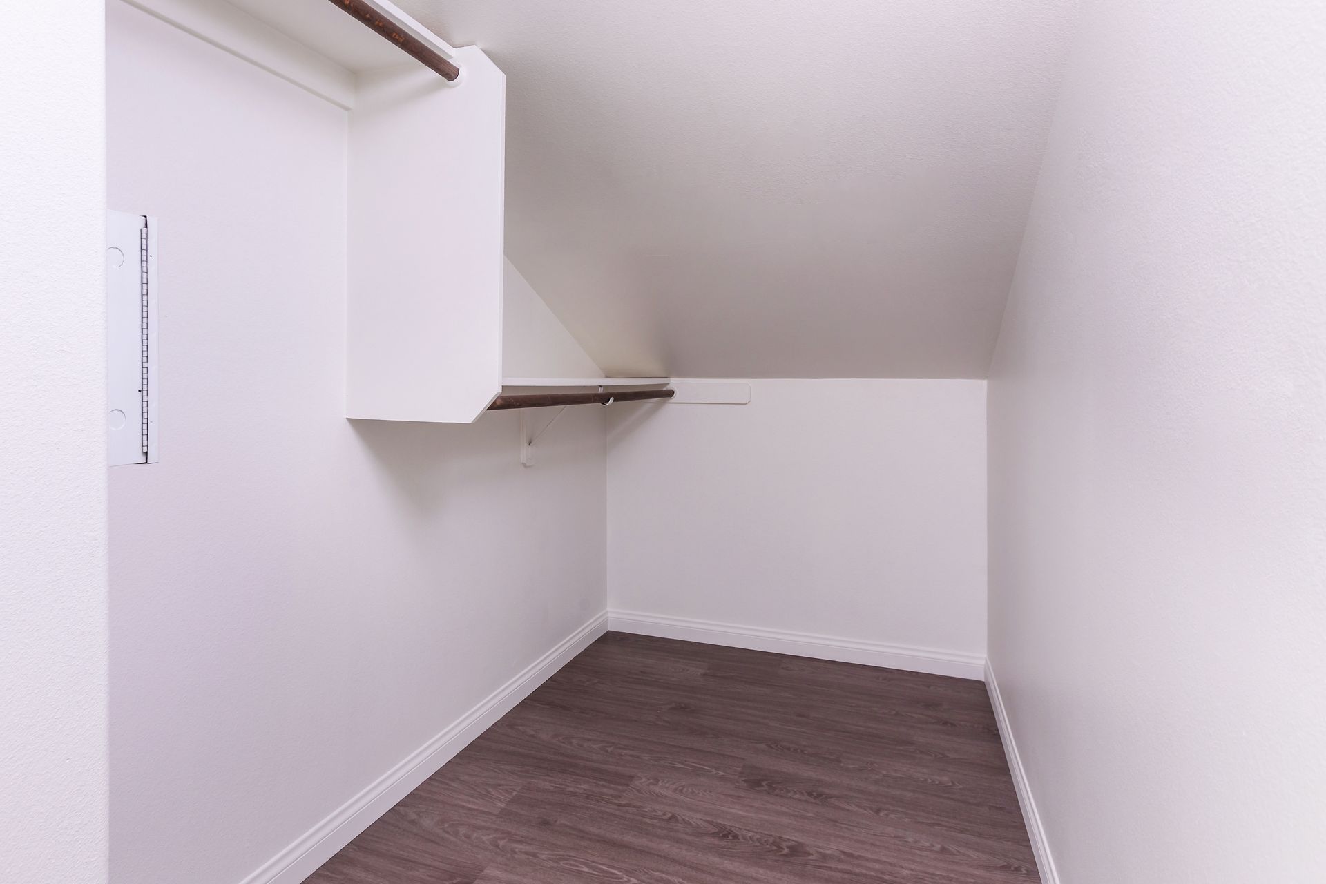 An empty walk in closet with white walls and wooden floors.