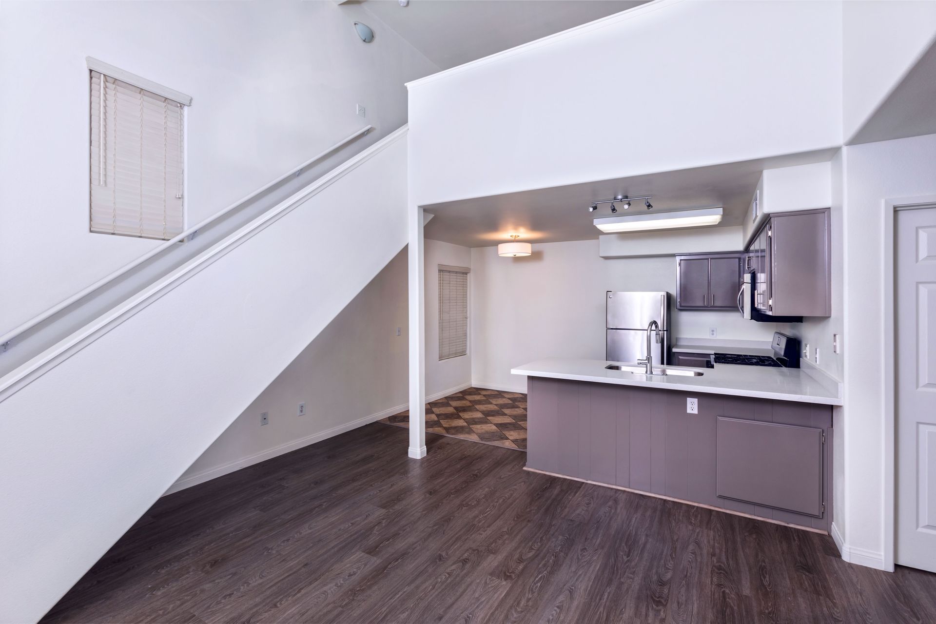 An empty apartment with a kitchen and stairs leading up to it.