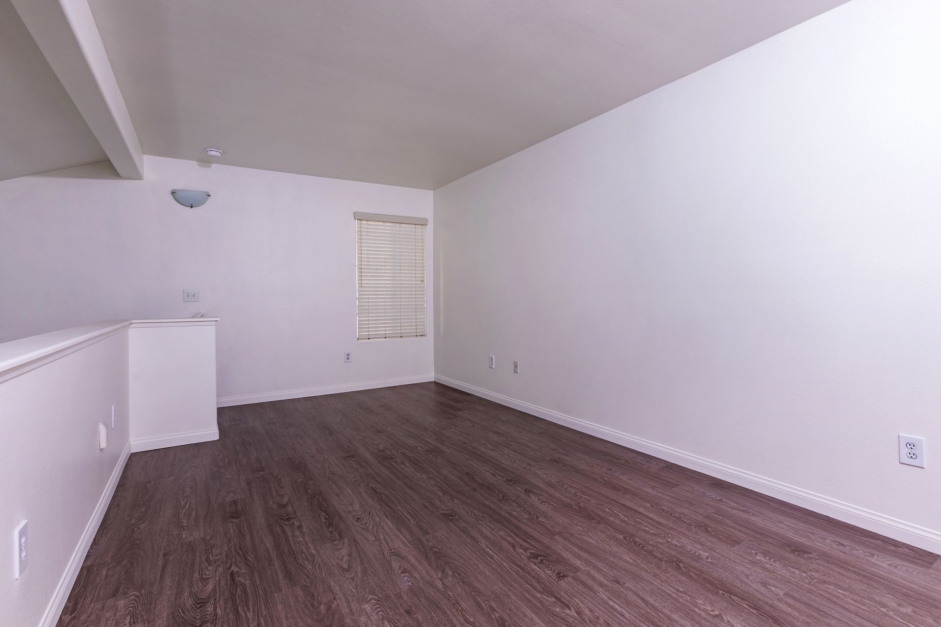 An empty living room with hardwood floors and white walls.