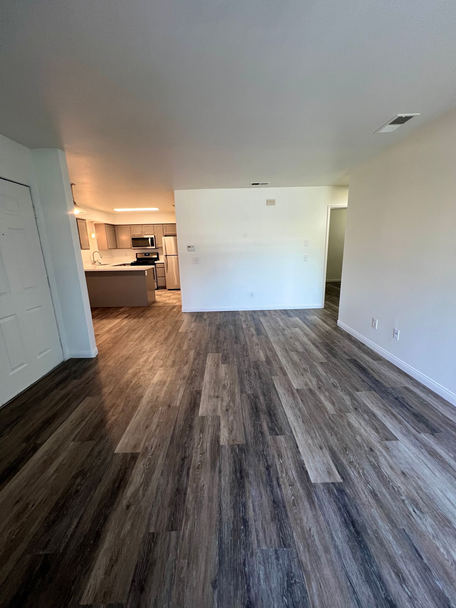 A living room with hardwood floors and a kitchen in the background.