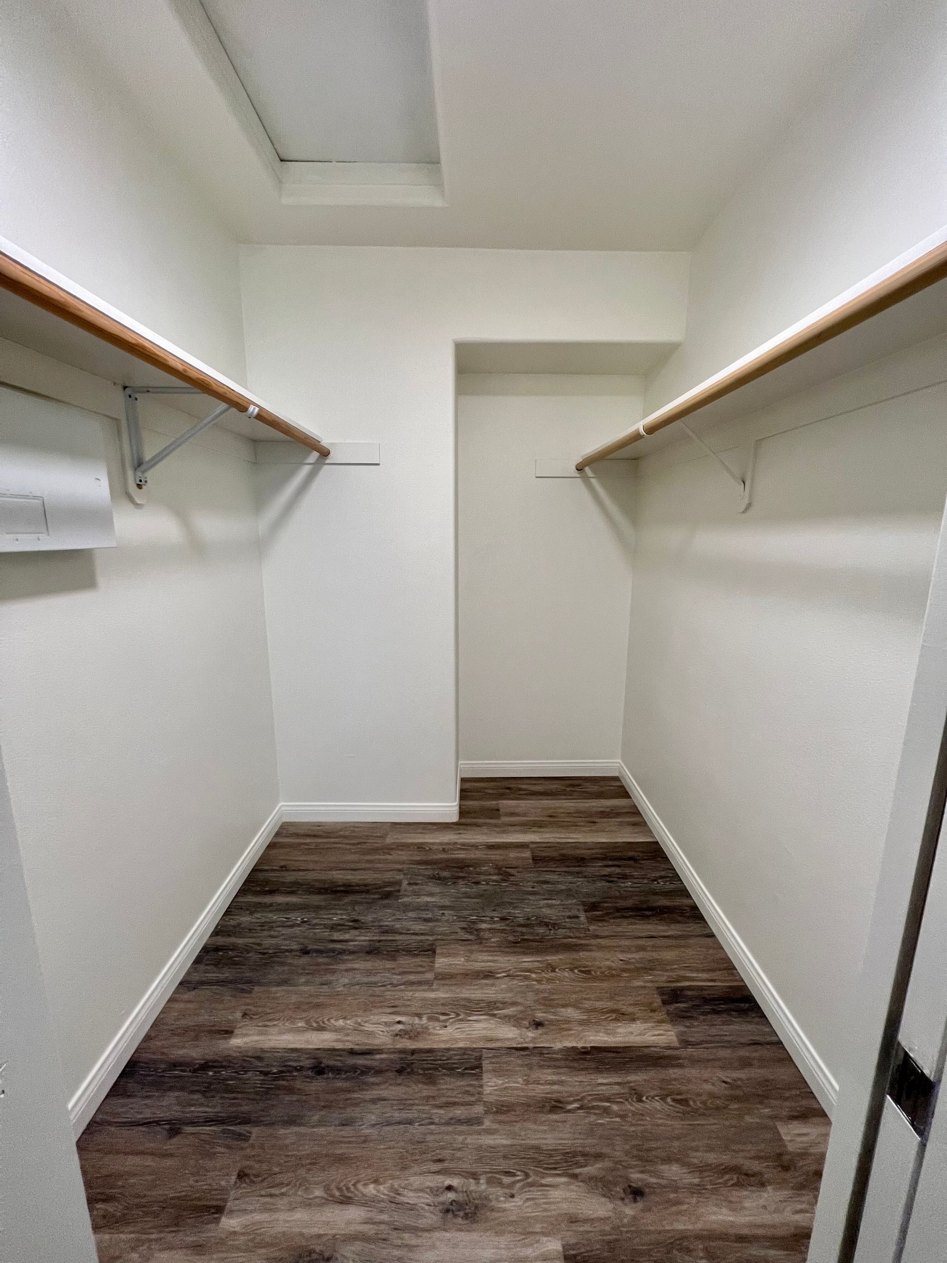 A walk in closet with wooden floors and shelves.