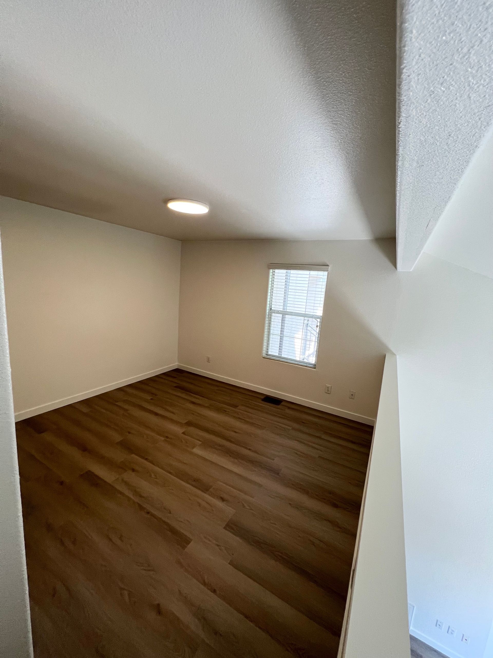 An empty room with hardwood floors and a window.