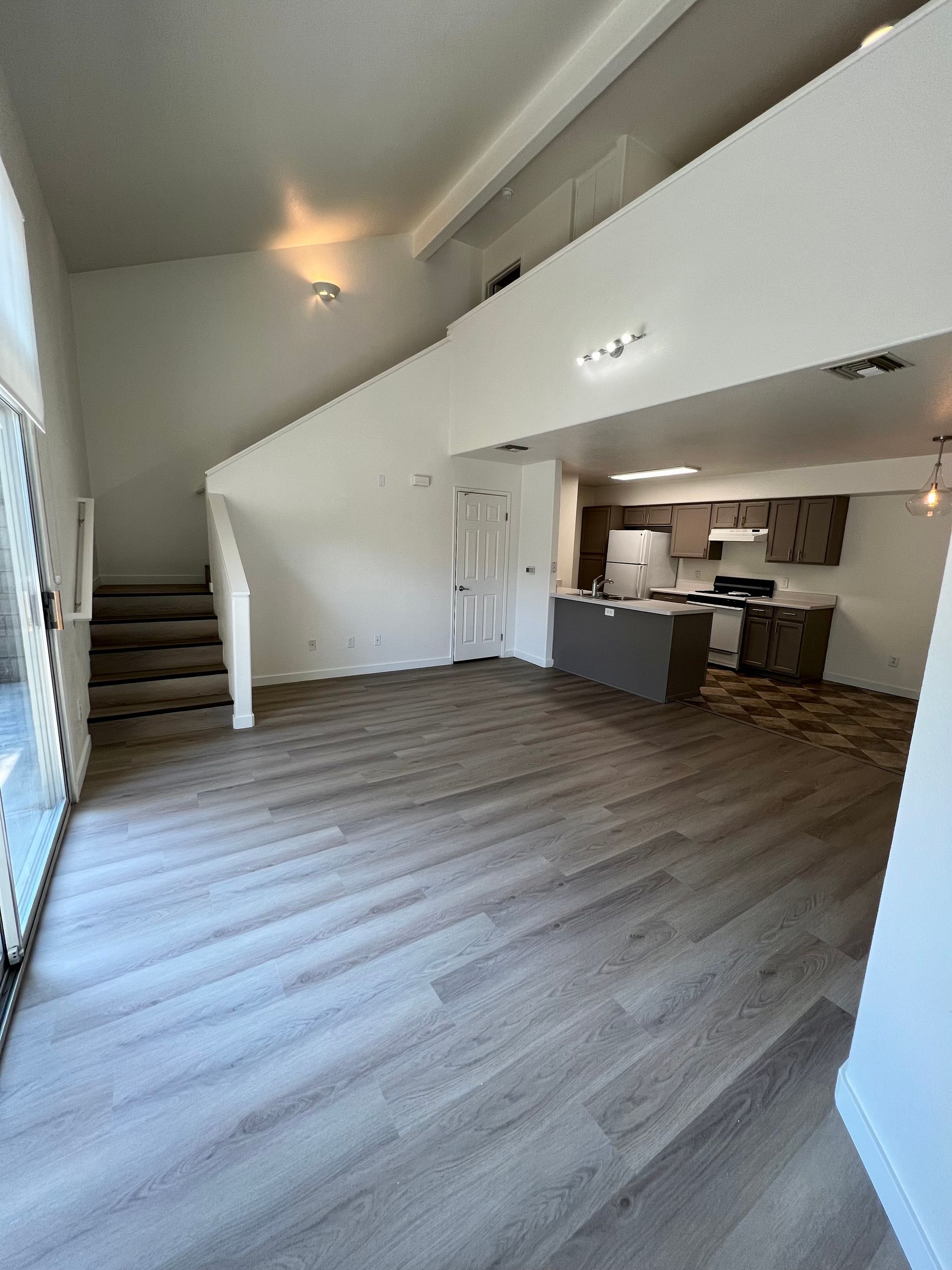 An empty living room with hardwood floors and stairs leading to the kitchen.