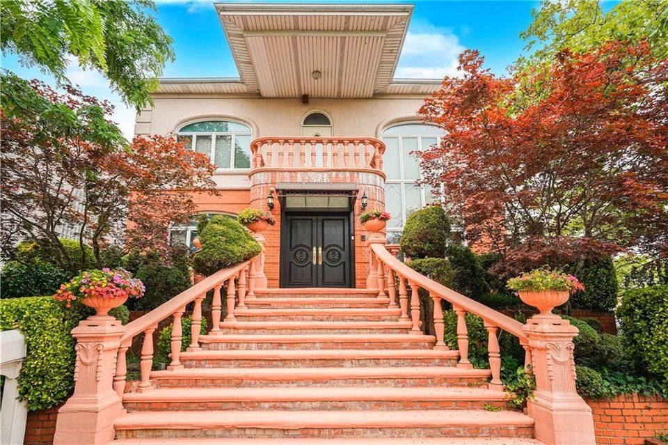 Pink-hued house with grand staircase, ornate details, and colorful landscaping.