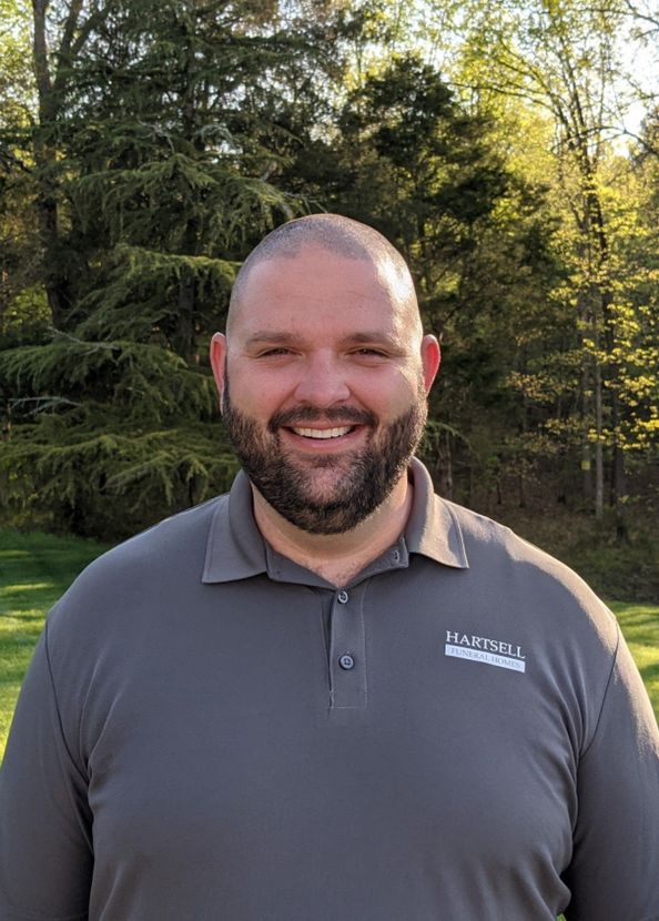A man with a beard is smiling for the camera in front of trees.