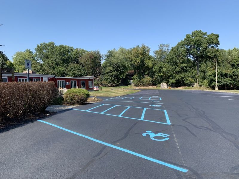 Parking lot with blue handicap parking spaces, building, and trees on a sunny day.