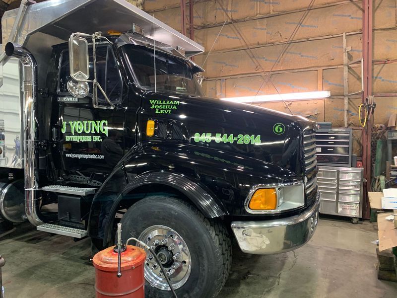 Black dump truck with silver accents inside a garage, next to a red oil can.