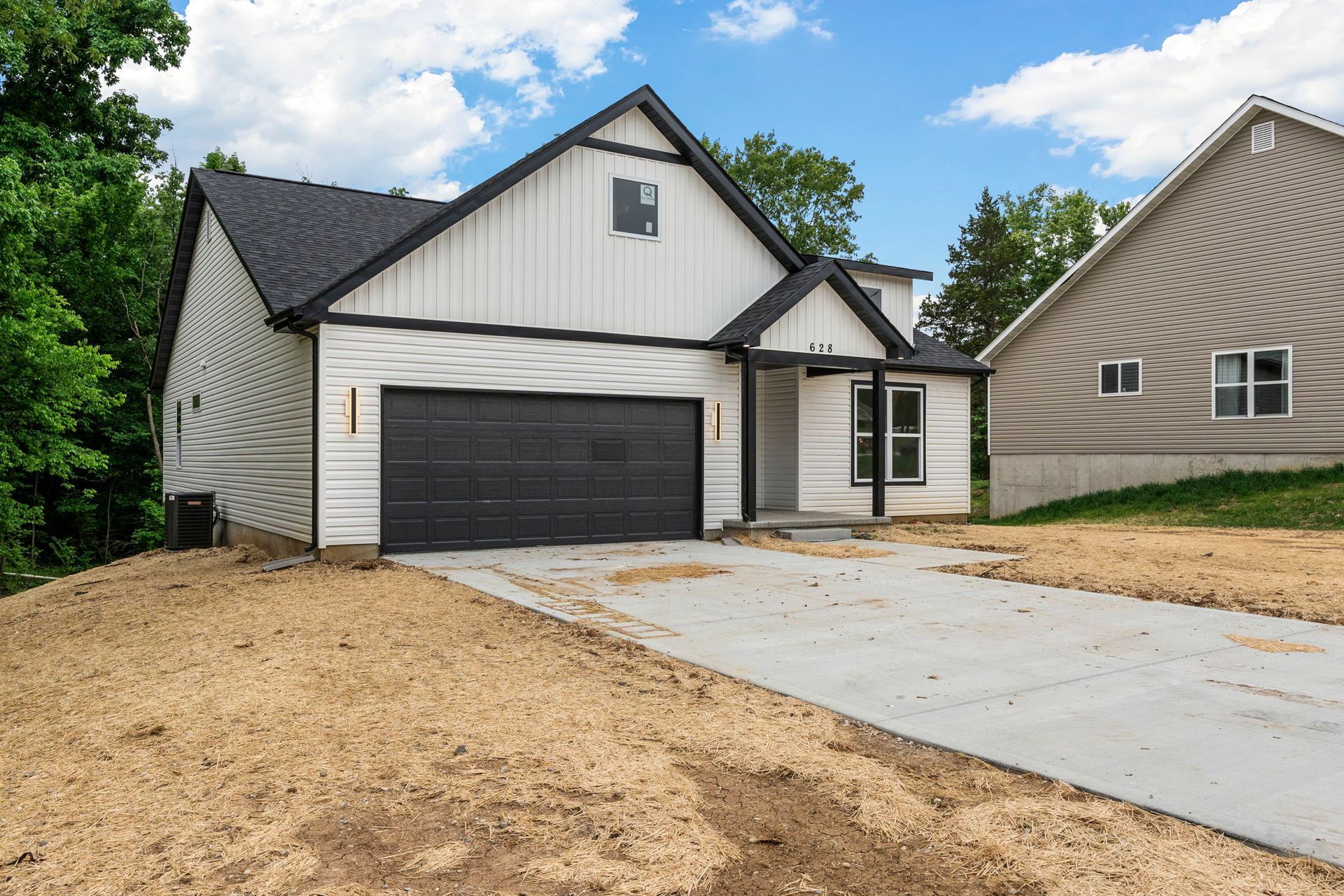 New white house with black garage door and driveway under construction, front exterior view