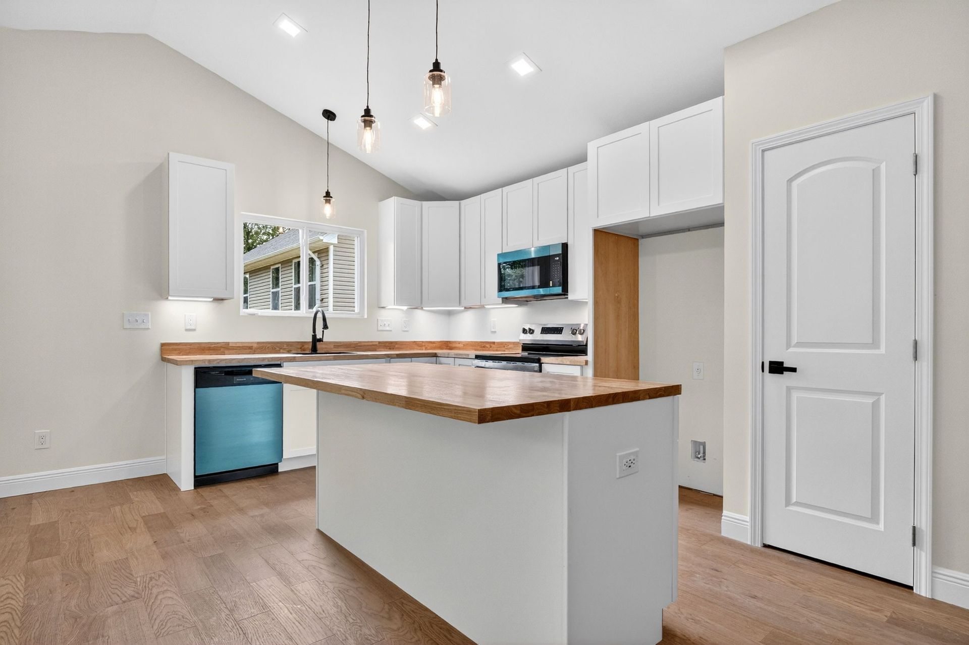 Bright modern kitchen with white cabinets, wood countertops, pendant lights, and a breakfast bar.