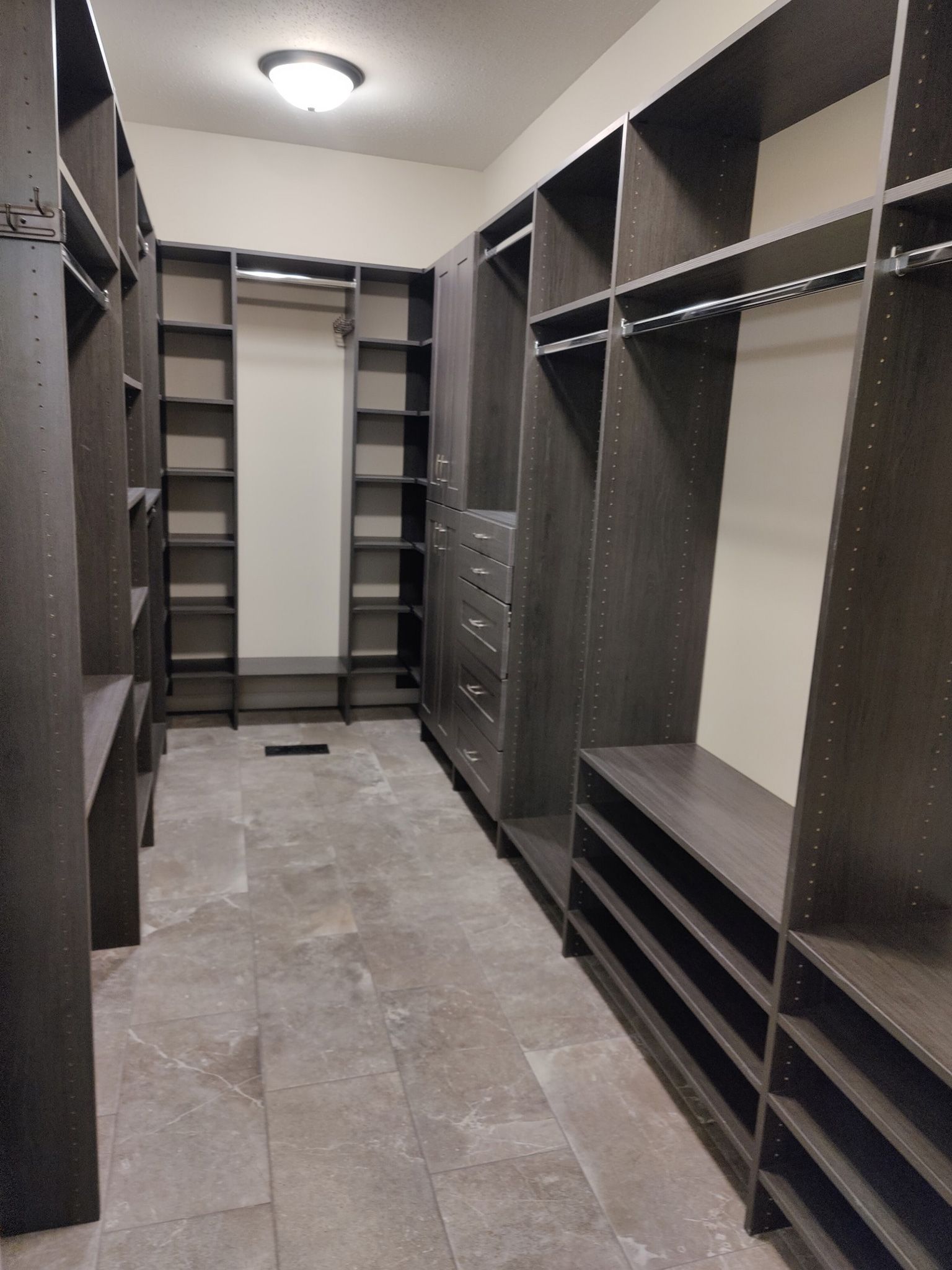 Empty walk-in closet with dark built-in shelving, hanging rods, and gray tile floor.
