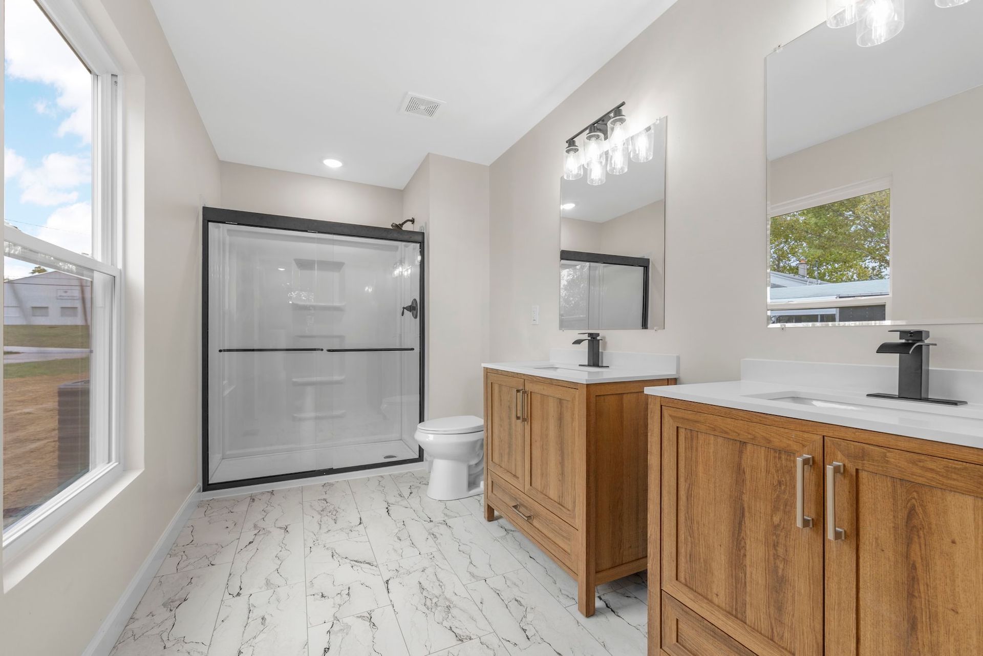 Bright modern bathroom with double wood vanity, large mirror, and glass shower enclosure
