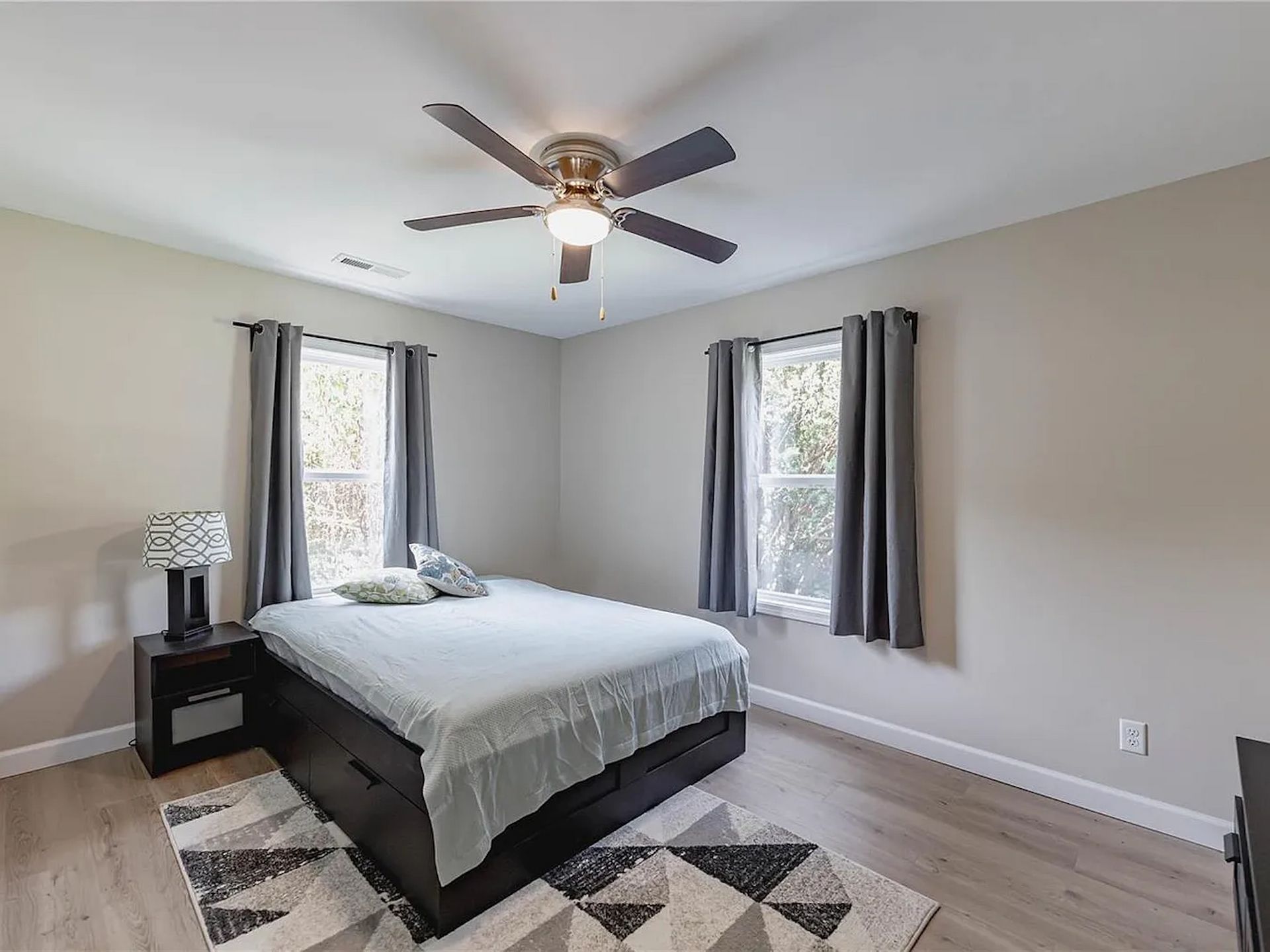 Bedroom with gray walls, dark wood bed, ceiling fan, and black-and-white geometric rug.