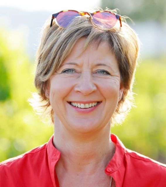 Eine Frau mit Sonnenbrille und rotem Hemd lächelt in die Kamera.