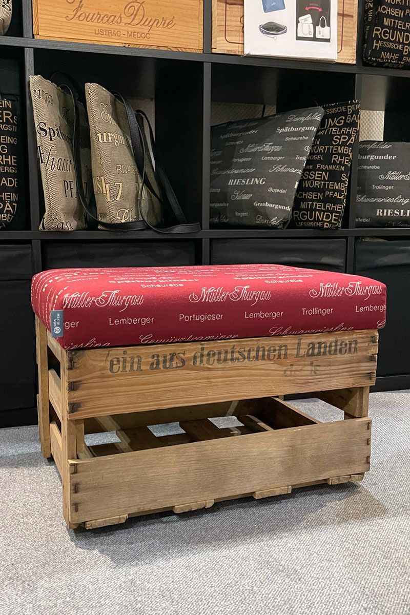 Eine Holzbank mit einem roten Kissen steht vor einem Regal voller Kissen.