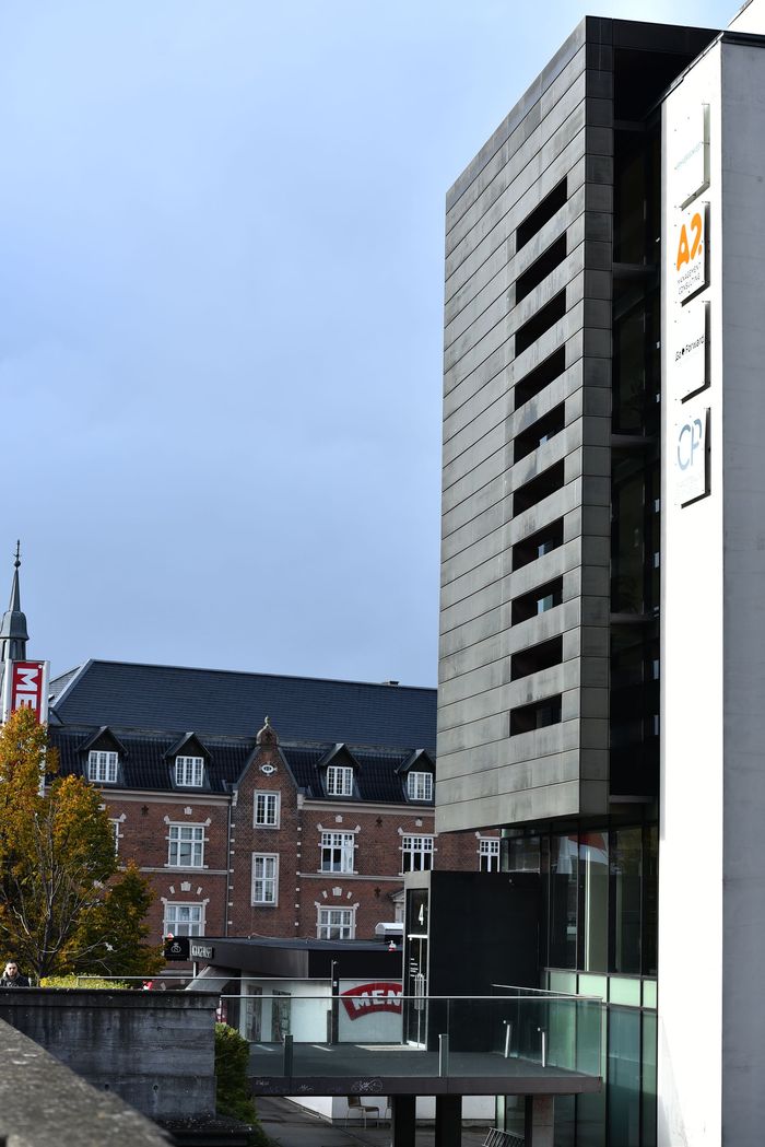 Moderne bygning med mørk facade, vinduer og tilstødende hvid bygning. Gammel murstensbygning i baggrunden. Det er Charlottenlund privathospital