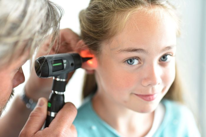 Læge undersøger et barns øre med et otoskop. Pigen smiler, mens undersøgelsen finder sted.