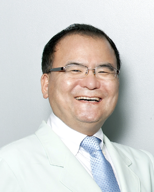 Man in white lab coat, smiling, wearing dark top. Light background.