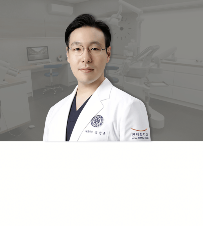 Doctor in white coat, glasses, stands in clinic setting.