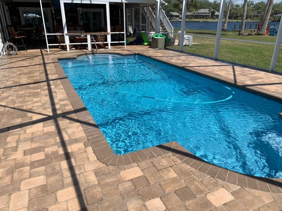 Pool with blue water, surrounded by brick pavers, screened porch in background.