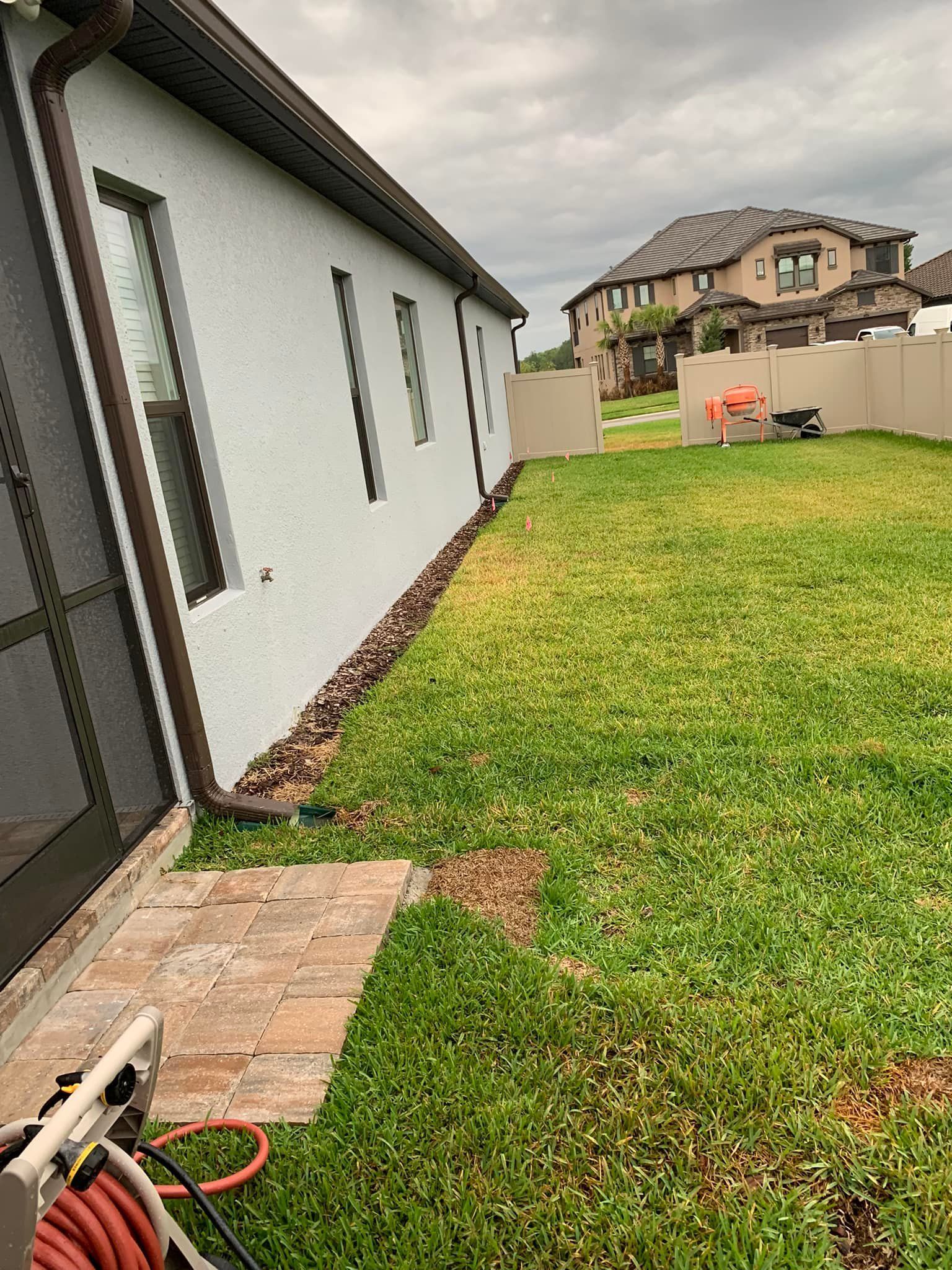 A house exterior with brown gutters, windows, and a grassy lawn with a cloudy sky.