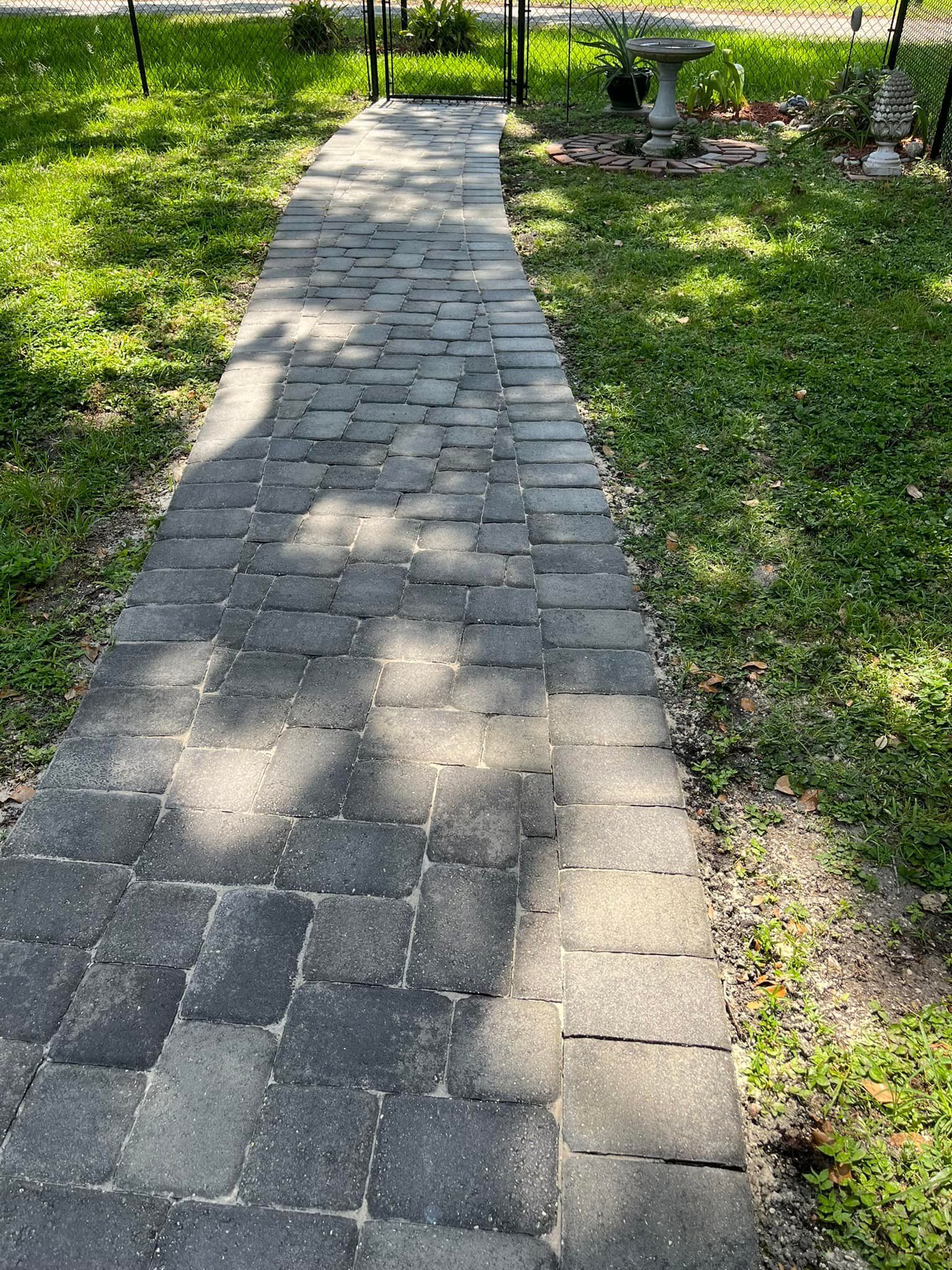 Brick walkway through grass towards a gate. Shady with dappled sunlight.