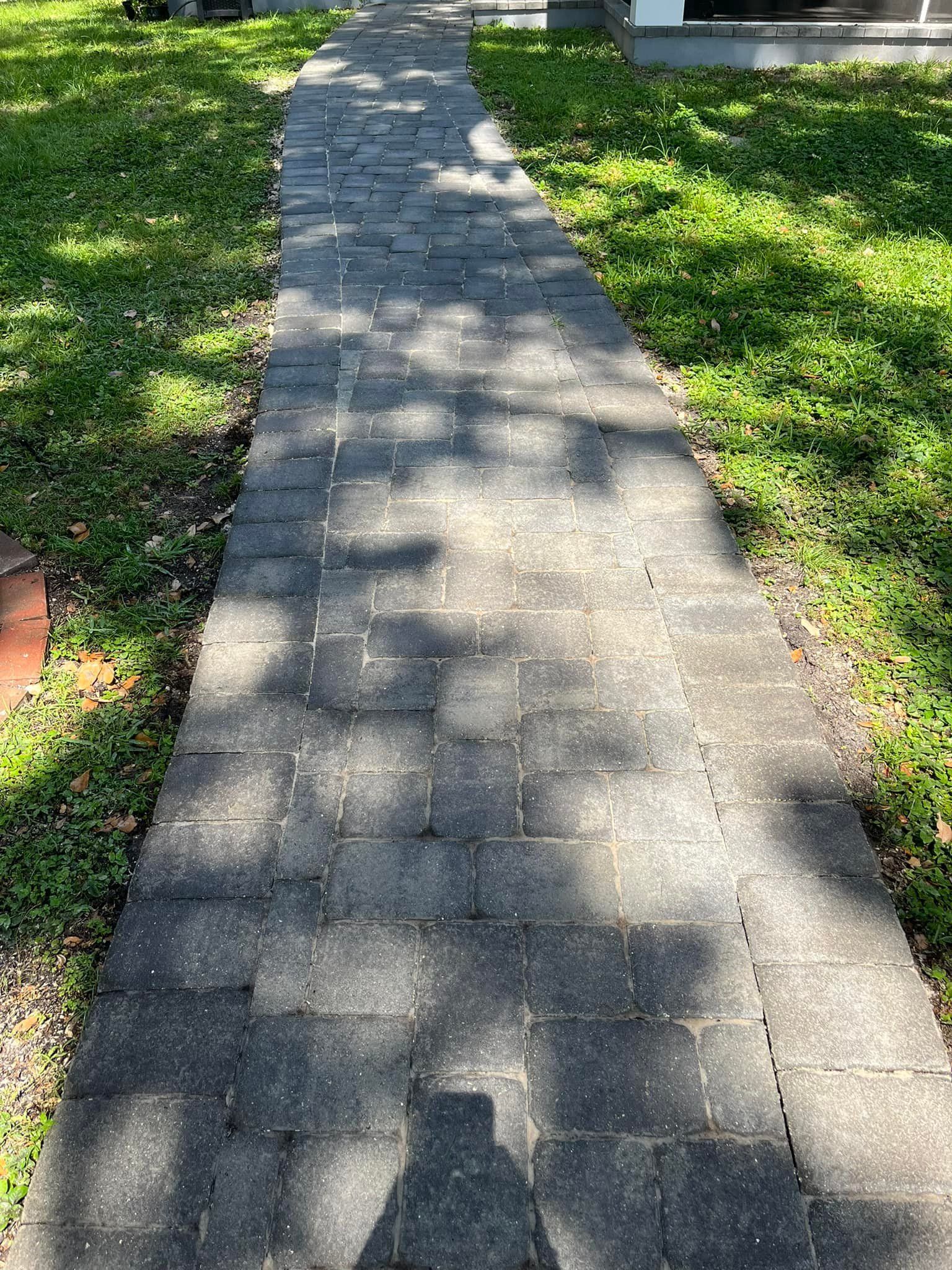 Brick walkway through green grass, shadows from trees overhead.
