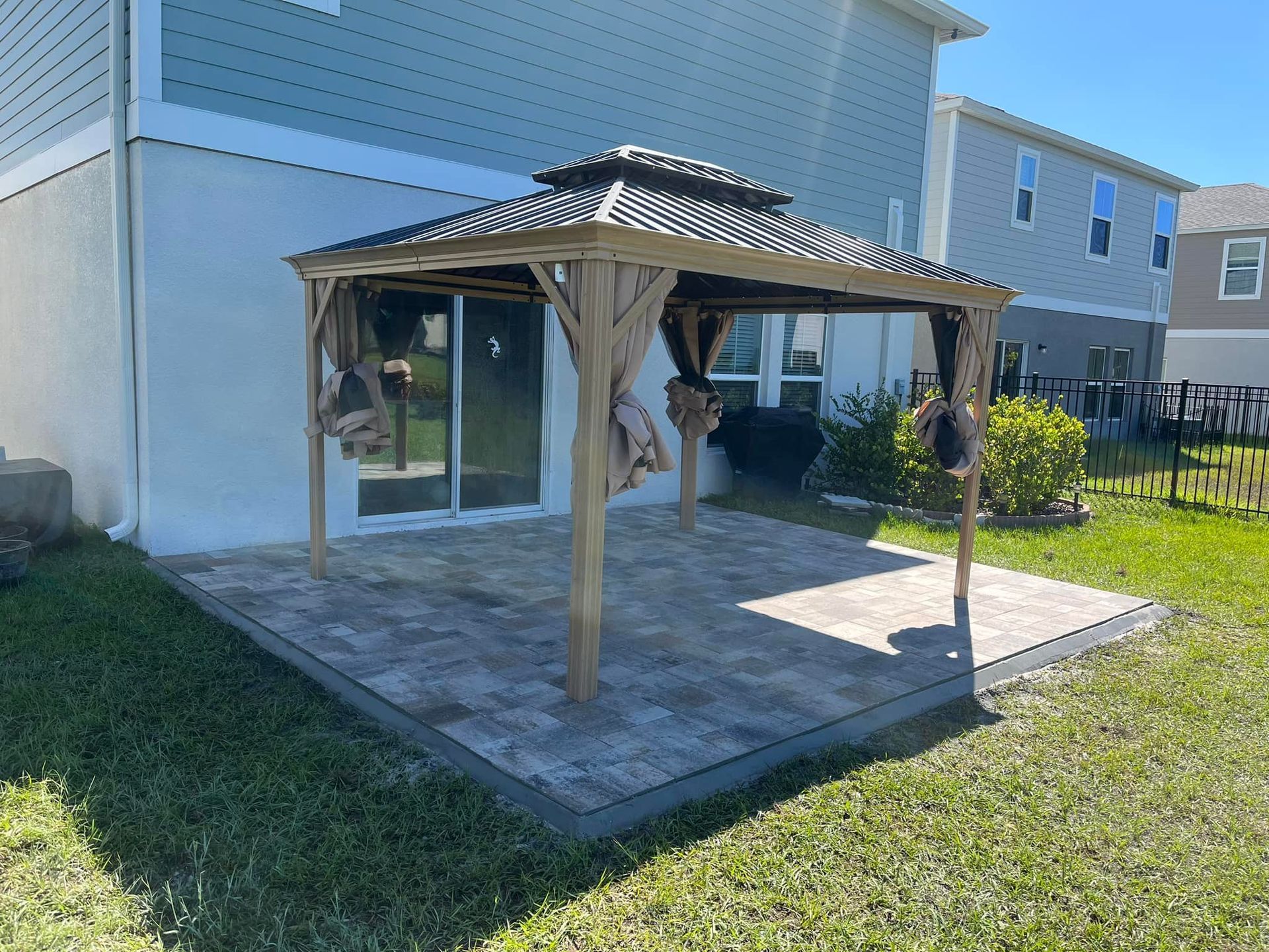Gazebo on a paved patio in a backyard with a house in the background.
