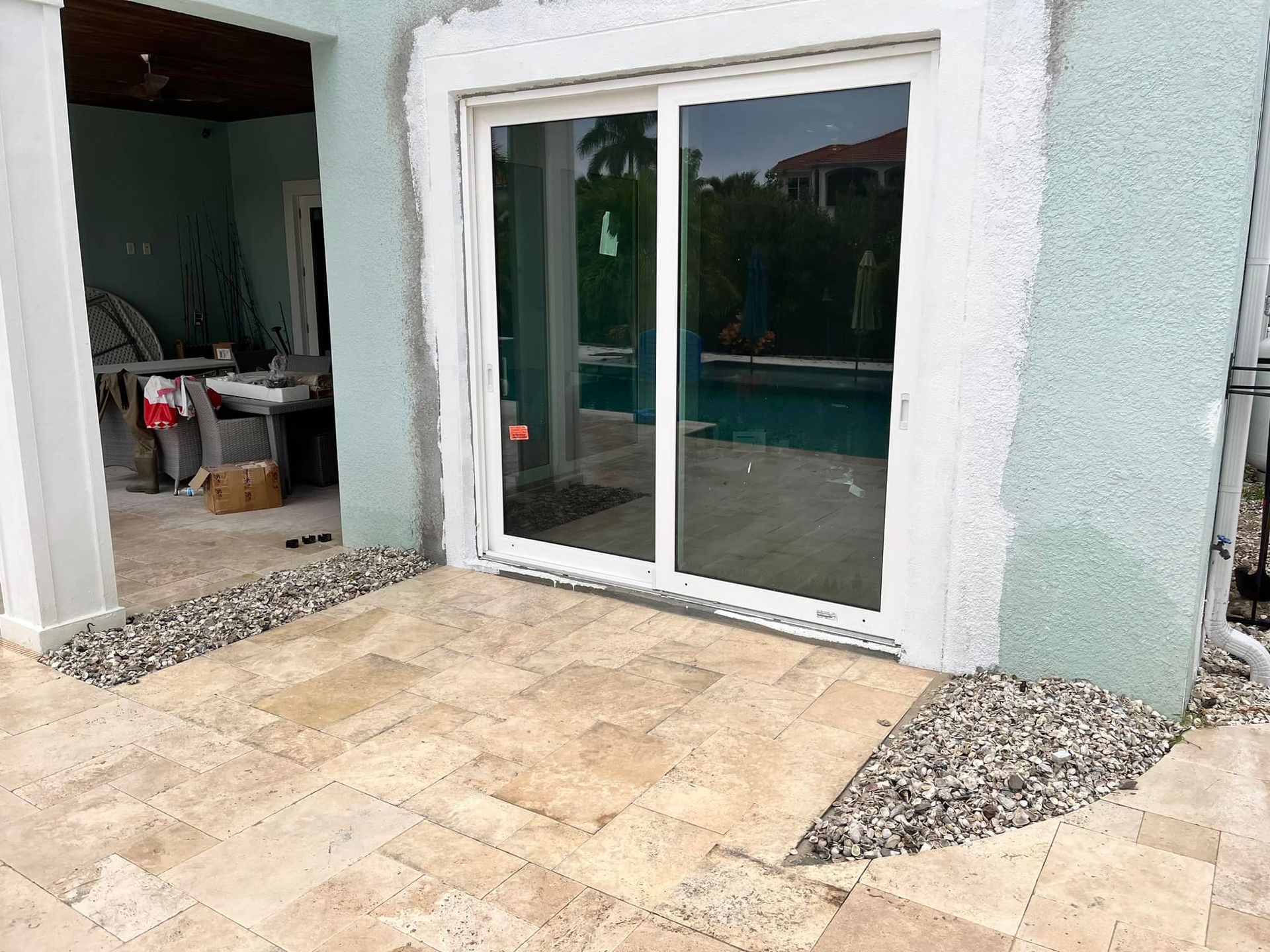 Patio with sliding glass door and pool visible. Beige tile floor, turquoise wall, and stone edging.