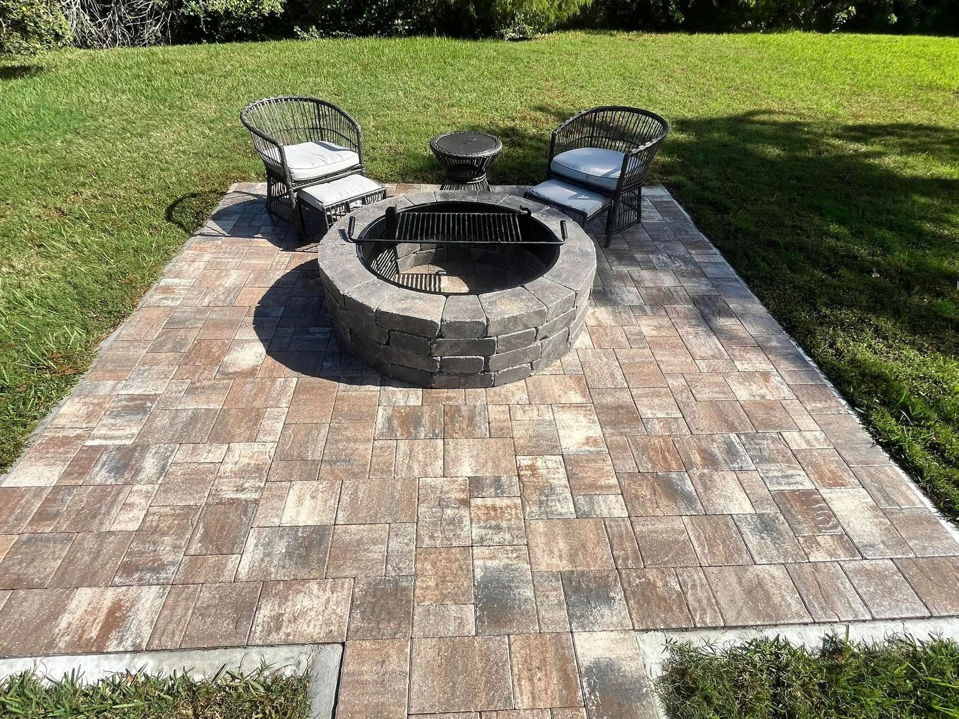 Fire pit area: stone pavers, fire pit, two chairs, small table, green grass.