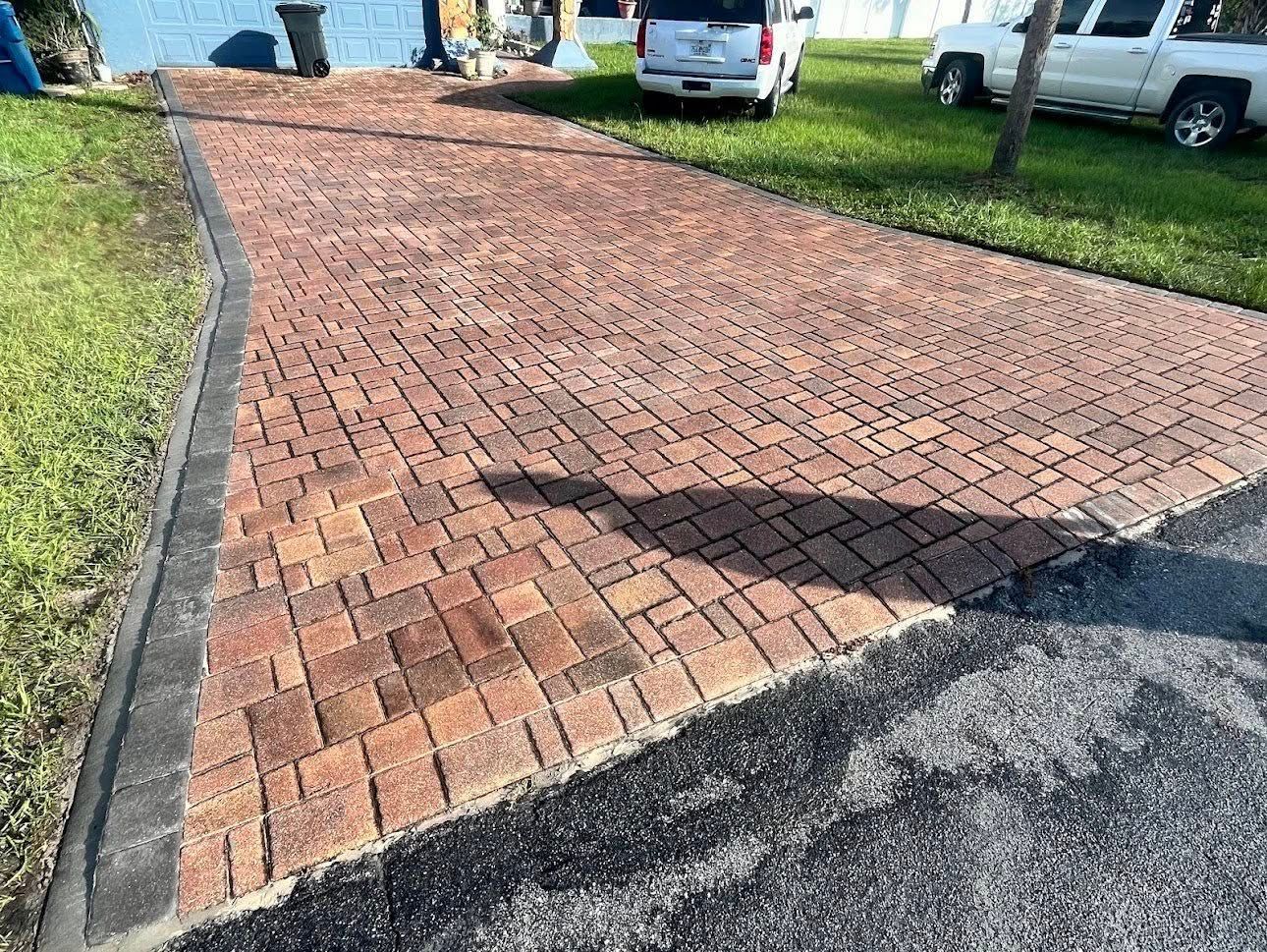 Brick-paved driveway leading to grass and cars; sunlight casts a shadow.