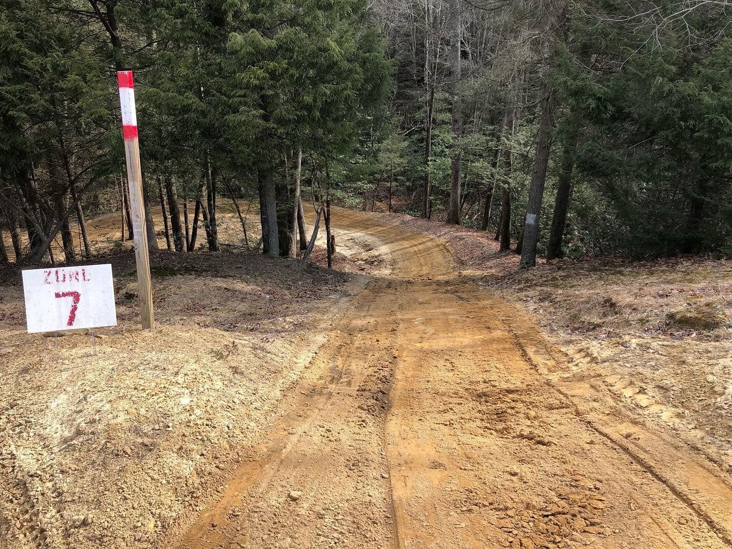 A dirt path leads into a wooded area, marked by a sign labeled 