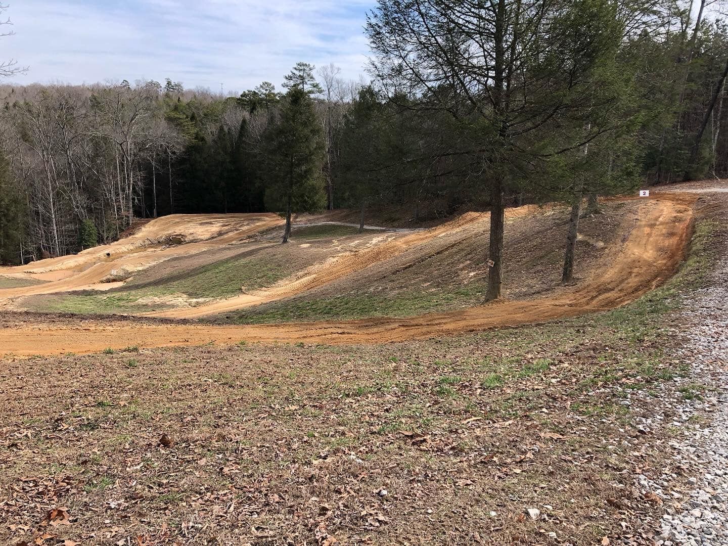 A dirt track curves through a grassy, wooded hillside under a bright sky.