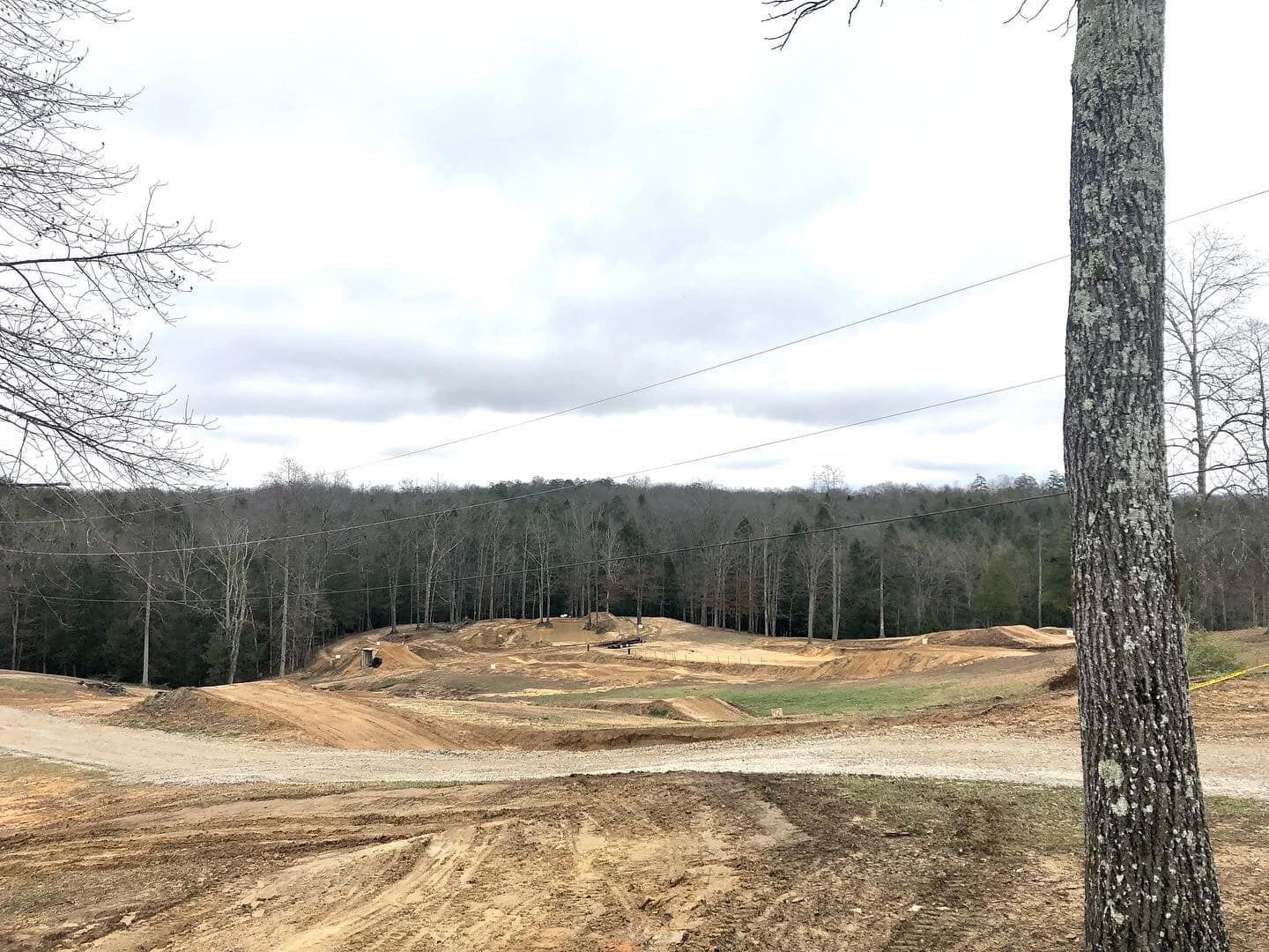 A dirt track winds through a clearing in a forest under a cloudy sky, seen from an elevated perspective.