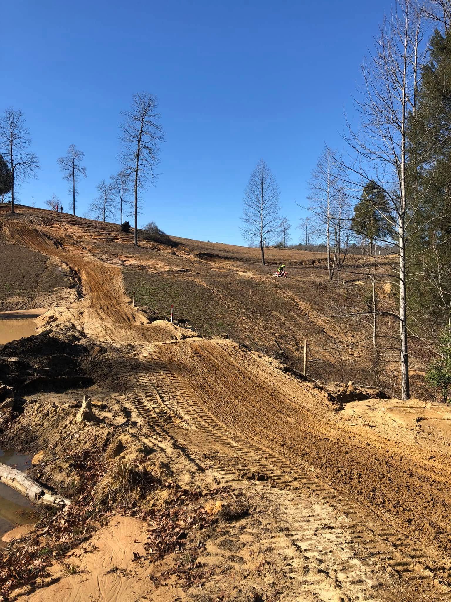 A muddy, cleared landscape with tire tracks on a dirt slope under a clear blue sky, showing signs of recent land leveling.