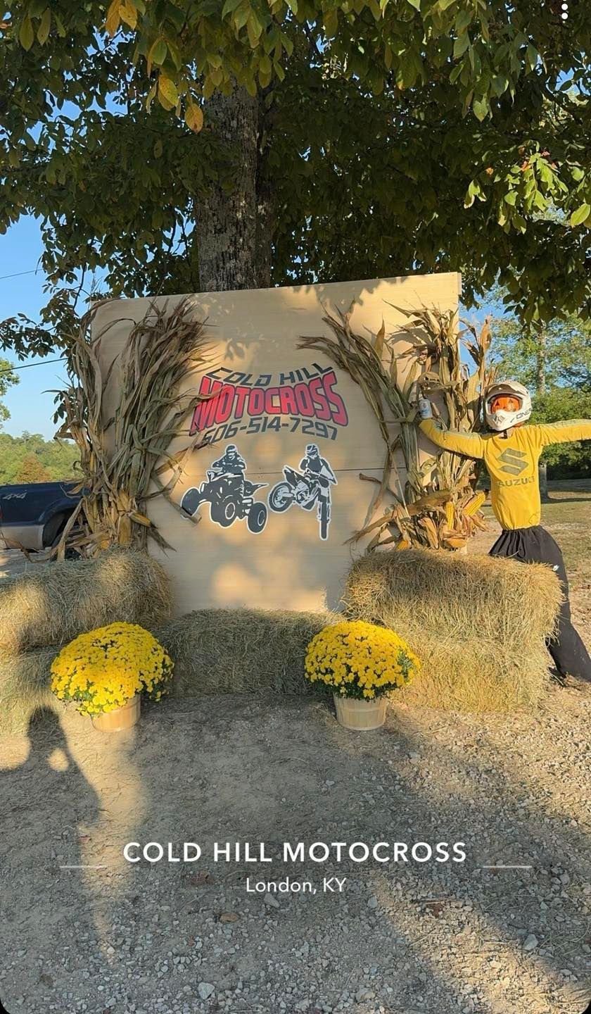 Cold Hill Motocross event display featuring a branded backdrop, hay bales, yellow mums, and a scarecrow in London, KY.