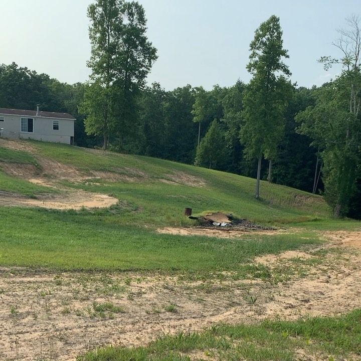 A grassy, hilly yard with exposed dirt patches and a small house on a rise under a clear sky.
