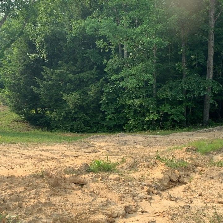 A dirt and gravel construction area leading toward a dense green forest on a bright day.
