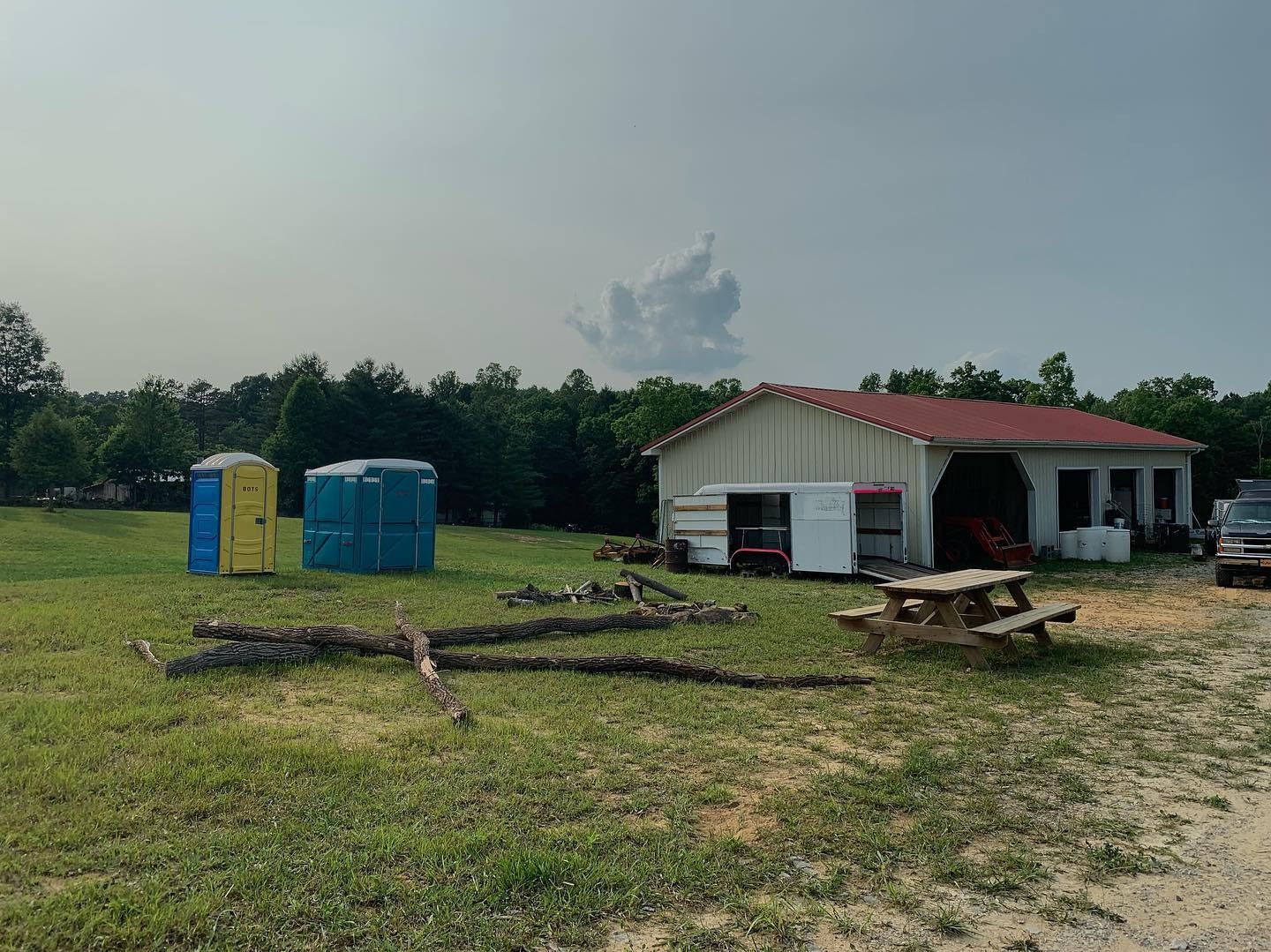 A yellow and a blue portable toilet stand in a grassy field next to a light-colored building with a red roof.