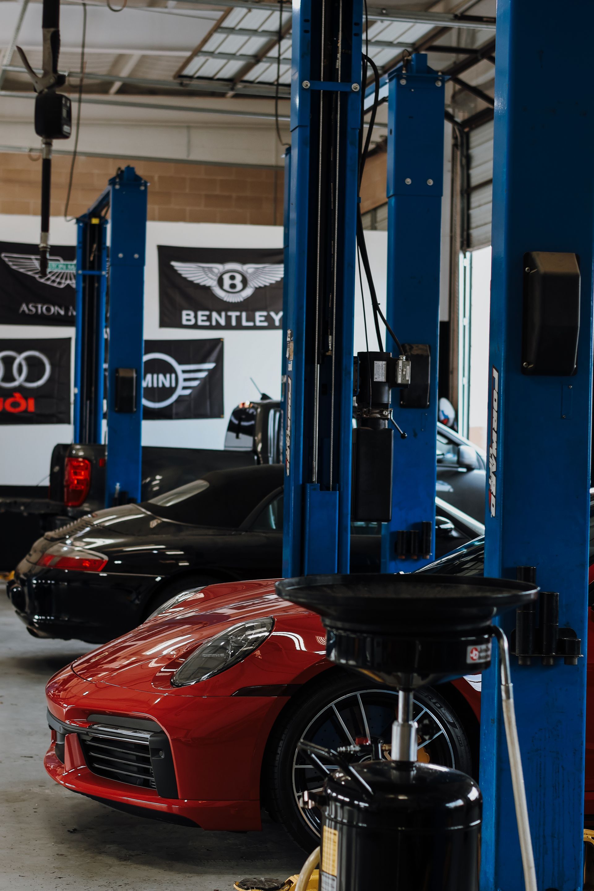 Red sports car and black car on lifts in auto repair shop with Bentley, Audi, and Mini flags. | Euro Auto Repair