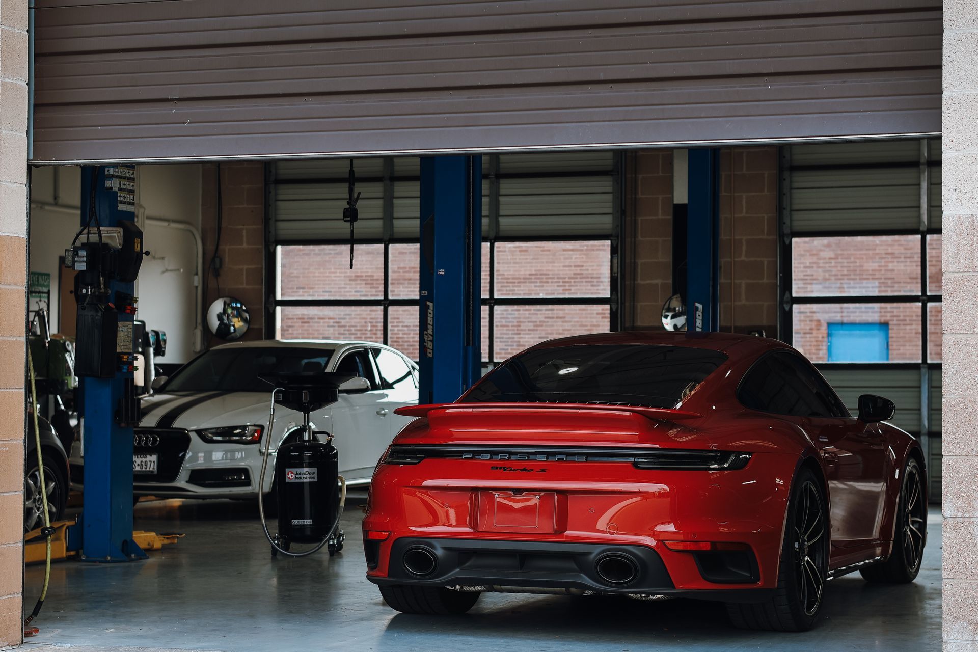 Red sports car inside a garage with a white car in the background and a partially open door. | Euro Auto Repair