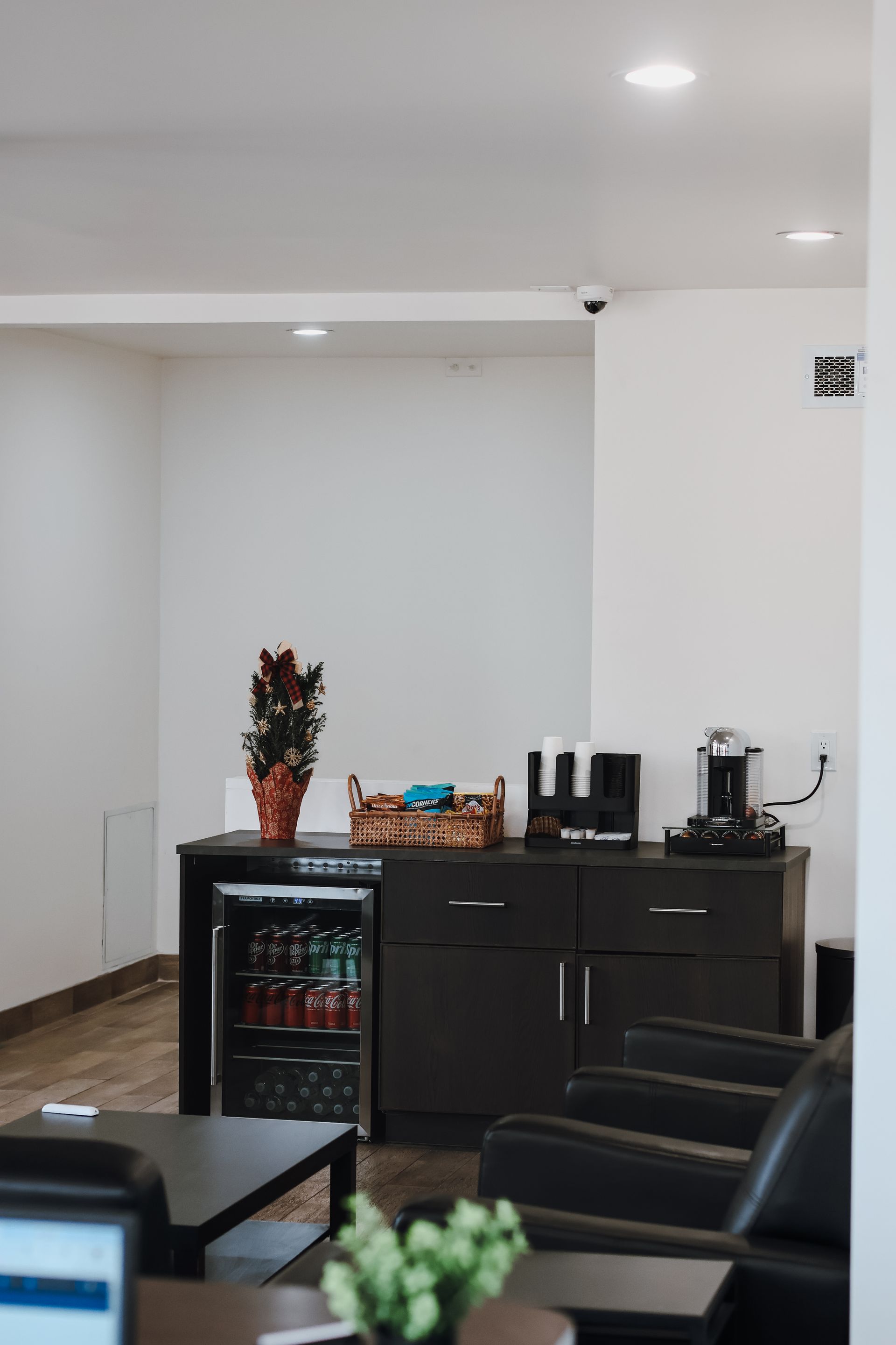 Interior with refreshment area; small refrigerator, coffee machines, seating, and decorative plants. | Euro Auto Repair